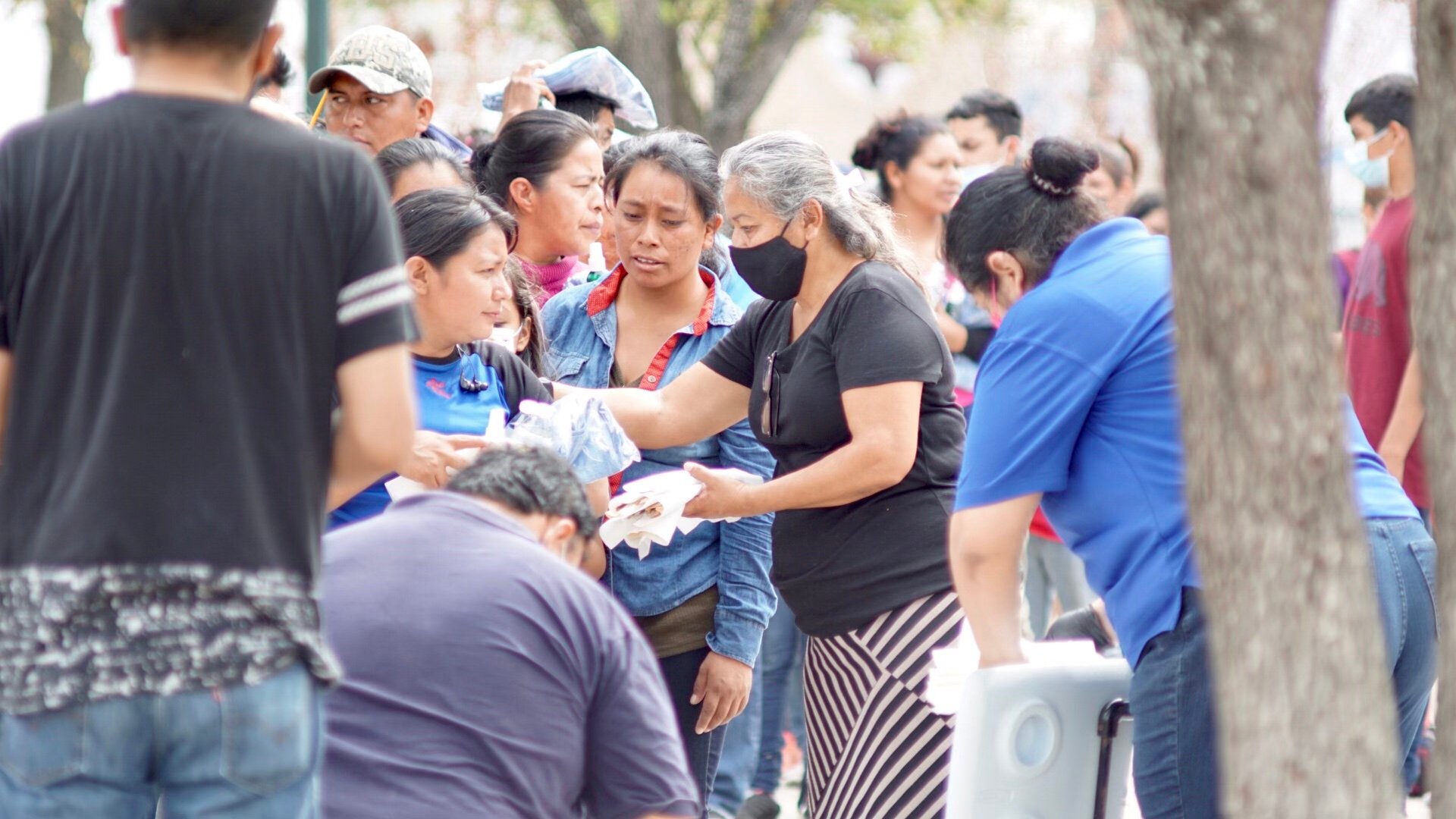 A woman with the Mercy Works Crisis Relief is wearing a mask and handing out supplies to a group of people gathered around.
